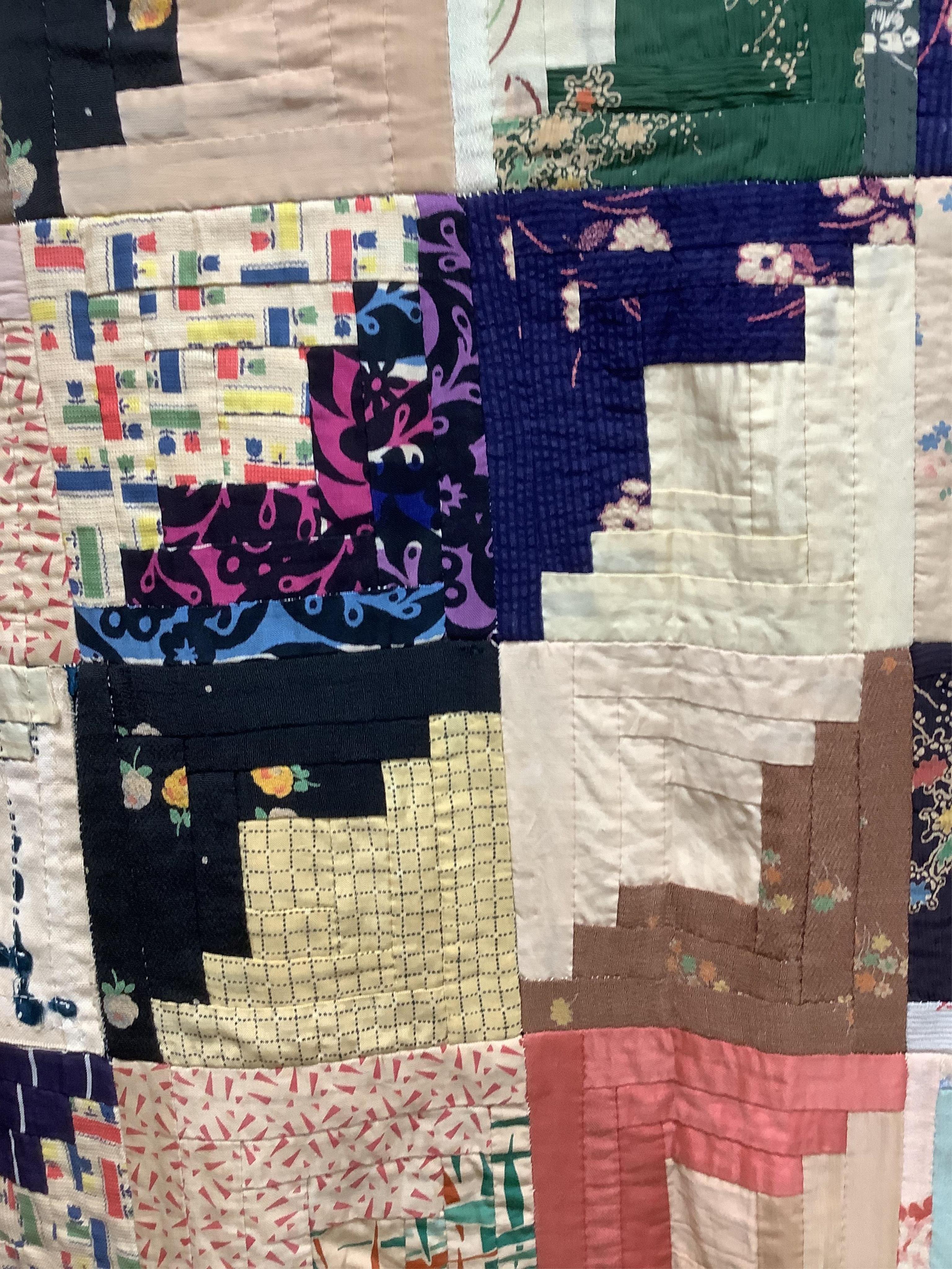 An early 20th century Log Cabin patchwork bedcover, worked in plain and printed silk, rayons and cottons from 1900 to 1940’s. Edged with a triangular patchwork border on three sides. Cover unlined. 158cm wide x 192cm lon